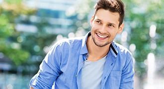 A young smiling man smiling outdoors while looking to the side