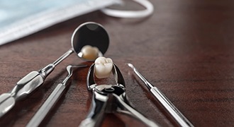 Dental forceps holding a tooth next to several other dental tools